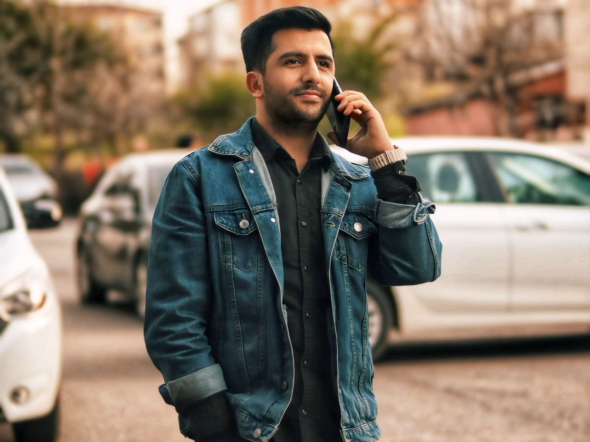Person taking a phone call in a lot beside parked cars